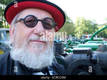 Elderly gentleman with a red hat and round eyeglasses visits a tractor show in Germany Stock Photo