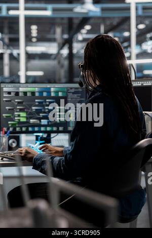 Data center call center agent providing logistics support to businesses, talking in headset mic. Worker in server room establishment overseeing node trees and communicating with engineers Stock Photo