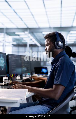 Engineer listening music, reconfiguring artificial intelligence server farm to optimize it for data processing requirements. AI expert wearing headphones ensuring data center operates efficiently Stock Photo