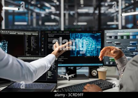 Data center technicians brainstorming, working together in office, using artificial intelligence computerized model. Server room coworkers collaborating, working with AI machine learning algorithms Stock Photo