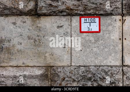 German hydrant location sign displaying h100 and 3.5 numbers, affixed to an aged stone and concrete wall, indicating the location of a hydrant in unde Stock Photo