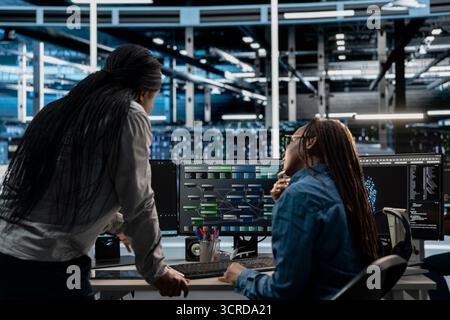 Technicians working together programming in server farm housing infrastructure storing datasets. IT experts collaborating, running code on PC to repair data center racks doing computational operations Stock Photo