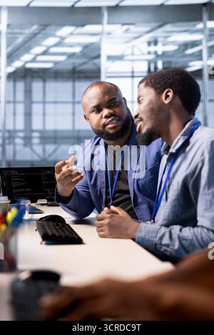 Data center admin discussing with coworker, using programming languages to construct algorithms and build applications. Server hub IT specialist talking with colleague, debugging and optimizing code Stock Photo