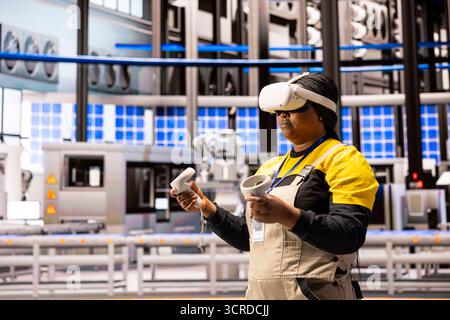 Industrial power plant technician wearing a VR headset and holding controllers participating in immersive training. Smart factory employee using virtual reality in overseeing manufacturing operations. Stock Photo