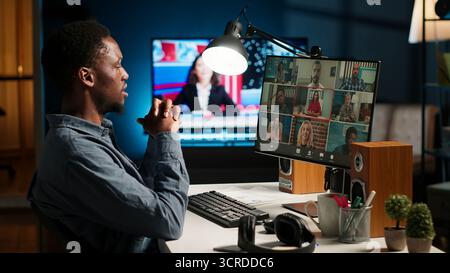 African American man and associates attending a virtual meeting call in his loft, discussing and communicating through a video conference, doing remote work at home. Camera B. Stock Photo