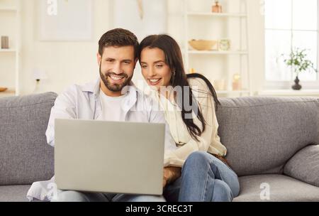 Happy laughing young couple watching laptop screen sofa sitting to enjoy funny movie, planning  Stock Photo