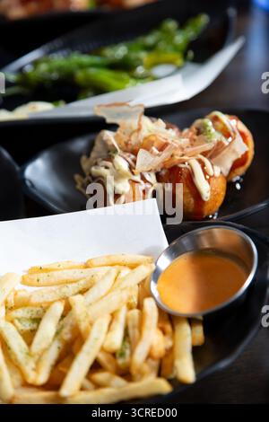 A view of a variety of appetizers, featuring seasoned french fries, takoyaki, and shishito peppers. Stock Photo