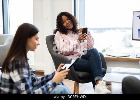 Two women using smartphones in a modern office setting Stock Photo