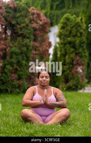 Woman in pink sportswear sitting on a grass on lotus pose and feeling good Stock Photo