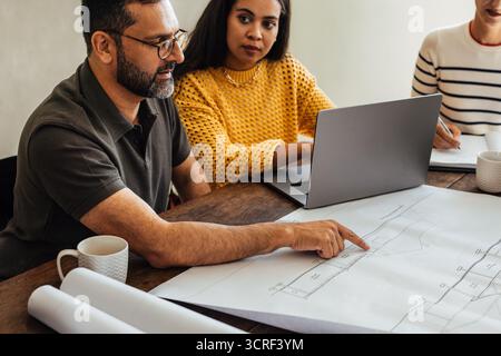 A diverse group of professionals, including a middle-aged man and a young woman, examining architectural blueprints and discussing a project around a Stock Photo