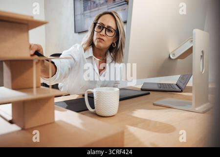 Architectural professional working on a model project at her office station with focus. Stock Photo