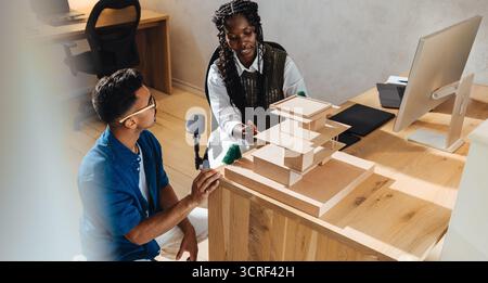 Two young architects discuss and develop plans over a detailed architectural model in a modern, bright office space, showcasing teamwork, creativity, Stock Photo