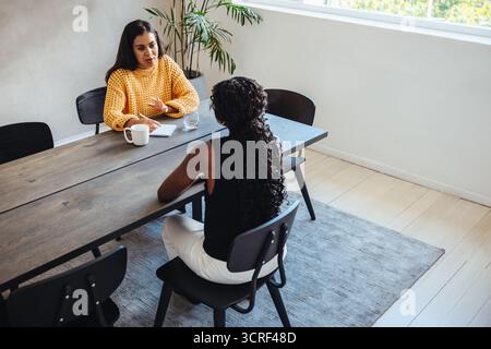 Two female professionals in their 30s having a collaborative business meeting in a modern office space with natural light. Professional and creative e Stock Photo