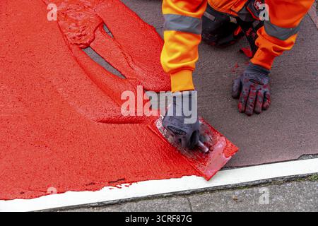 Application of red road surfacing on a cycle lane, inner-city road, so-called cold plastic surfacing, in the colour traffic red, RAL3020, the coloured Stock Photo