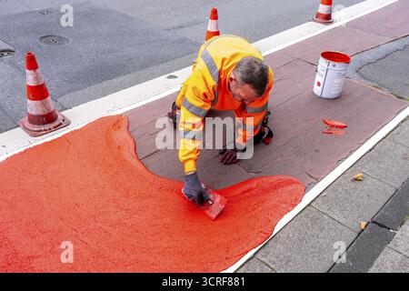 Application of red road surfacing on a cycle lane, inner-city road, so-called cold plastic surfacing, in the colour traffic red, RAL3020, the coloured Stock Photo