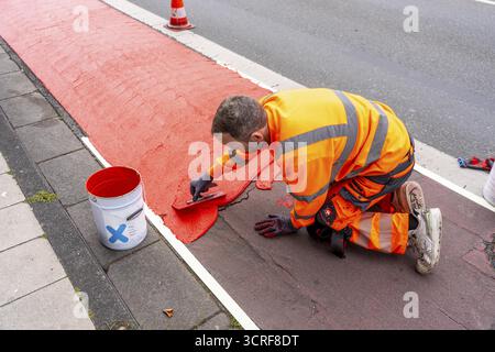 Application of red road surfacing on a cycle lane, inner-city road, so-called cold plastic surfacing, in the colour traffic red, RAL3020, the coloured Stock Photo
