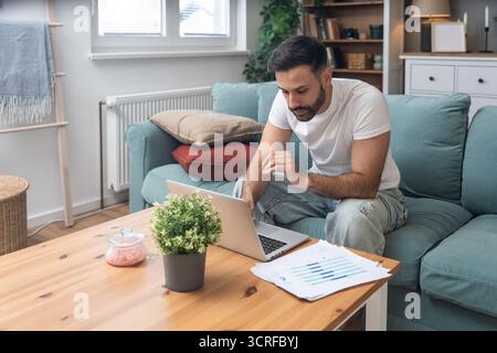 Young university student, freelancer business man, working at home on laptop computer, testing new innovative technology and online internet tools whi Stock Photo