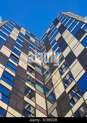 Modern skyscraper facade viewed from the ground, featuring a repeating geometric checkerboard pattern of dark panels and reflective blue glass windows Stock Photo