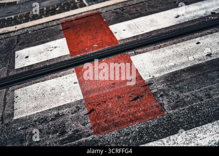 Urban street asphalt surface featuring a pedestrian crosswalk with white and red stripes, intersecting with dark tram tracks, creating an abstract tex Stock Photo