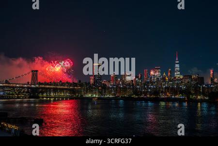 July 4th. View of vibrant fireworks exploding over the dark waters reflecting city lights, illuminating the skyline and bridge in New York, New York, Stock Photo