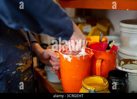 Hands of a screen printing artisan mixing inks in orange buckets. Color preparation and mixing for textile printing and screen printing. Detail Stock Photo