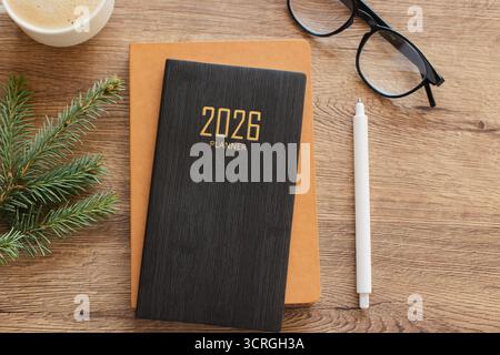 A tidy workspace featuring a 2026 planner, spiral notebook, white pencil, glasses, and a cup of coffee on a warm wooden desk, suggesting planning, foc Stock Photo