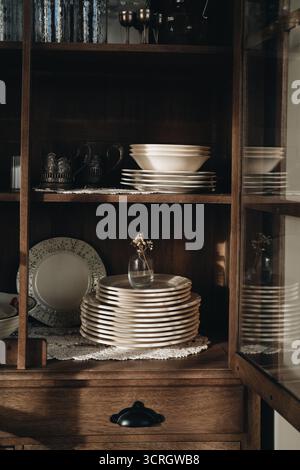 stack of vintage plates crockery pottery on a shelf in a wooden cupboard with a soft warm sunlight. Aesthetic lifestyle photo Stock Photo