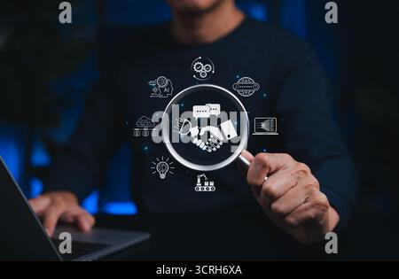 AI and human collaboration concept. Person holds magnifying glass focusing on handshake between robot and human, surrounded by technology icons, Stock Photo