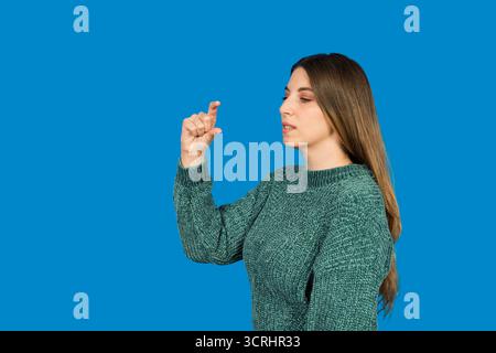 Woman making a tiny hand gesture against a blue background, indicating something small Stock Photo