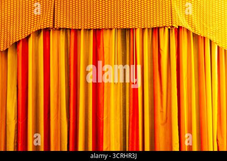 Curtains of red-yellow color in soft light, close-up. Stock Photo