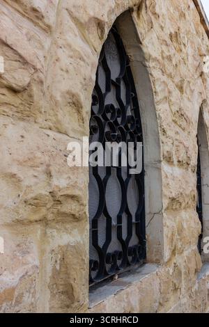 Rustic Stone Wall With Arched Window And Decorative Iron Bars On Exterior Building Stock Photo