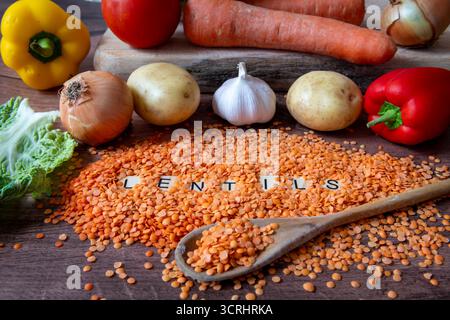 A heap of split red lentils on a kitchen work top and in a wooden spoon with a selection of vegetables. Stock Photo