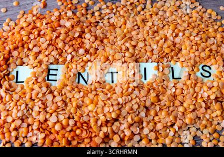 Close up of the word lentils emerging from a heap of split red lentils. Stock Photo