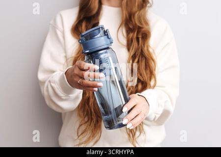 Woman holding reusable blue water bottle. Healthy hydration and eco friendly lifestyle. Minimal clean background with wellness concept. Stock Photo