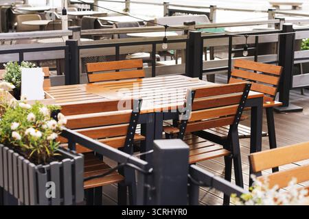 Outdoor terrace with wooden tables. Restaurant seating area with chairs. Cozy dining place in sunlight. Modern furniture for hospitality service. Stock Photo
