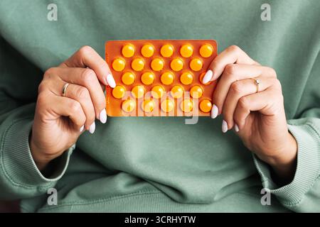 Woman holding blister pack of yellow tablets. Medicine and health supplement concept. Pharmacy product in female hands. Healthcare with vitamins. Stock Photo