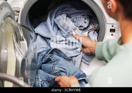 Clothes placed inside washing machine. Denim jeans in laundry drum. Household cleaning with textile fabric. Daily wash process at home. Washing jeans. Stock Photo