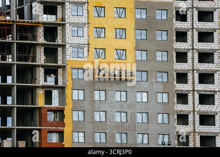 Construction workers on a suspended platform plaster and insulate the exterior facade of a multistory apartment building, illustrating urban renovation and energy-efficient progress Stock Photo