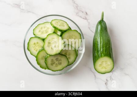 Fresh green cucumber slices in a glass bowl. Cut in half cucumber and bowl of juicy slices over marble countertop. Low calories snack vegetarian salad Stock Photo