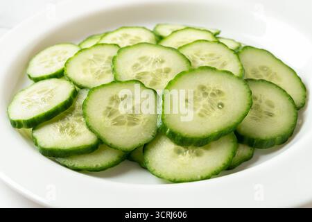 Juicy fresh cucumber slices on a white plate. Organic vegetables, cooking vegetarian food, low calories snack of raw veggies concept. Close-up. Stock Photo