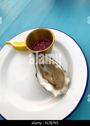 Single opened oyster served with fresh lemon slice and tangy sauce on coastal-themed setup. Ideal portrayal of seafood. Stock Photo