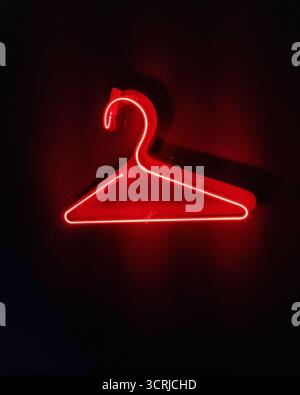 Hanger glowing red neon sign on black - wardrobe dressing room icon in dark room. Stock Photo