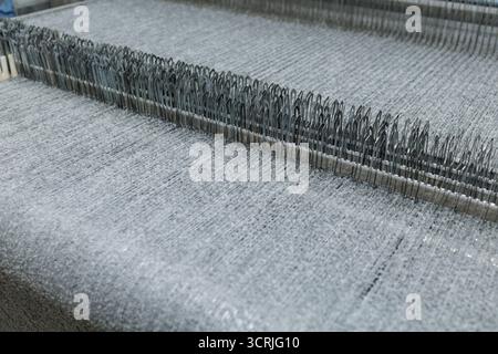 Close view of boucle loop fabric on industrial needles in a textile factory highlighting texture upholstery and fashion manufacturing Stock Photo