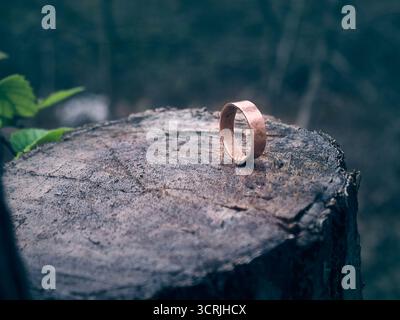 Handmade hammered copper ring on a wet tree stump in a forest. Stock Photo