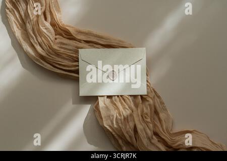 White envelope with grey wax seal on beige fabric and white background, soft shadows, flat lay Stock Photo