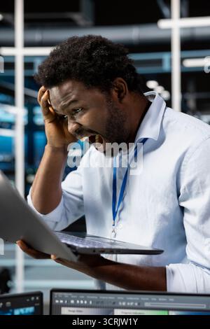 Upset server room technician screaming after making mistake and deleting all data backups. Livid man in data center raging after malfunction provoked by technical errors, unable to do system recovery Stock Photo