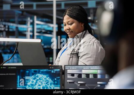 Smiling technician in data center uses AI technology for machine learning workloads. Happy server hub facility worker using artificial intelligence to perform demanding computing tasks Stock Photo