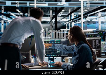 Data center team leader supervising technician setting up machine learning systems handling information. Supervisor oversees employee training neural networks to improve server farm operations Stock Photo