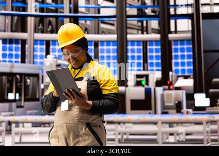 Factory manager attentively using tablet to oversee production processes in an industrial setting. Black female software expert implementing system updates to optimize warehouse workflow. Stock Photo