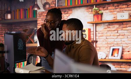 Team of startup workers conducting code review on PC to fix bugs, identifying technical issues with artificial intelligence company software. IT staff members optimizing code using device, camera B Stock Photo